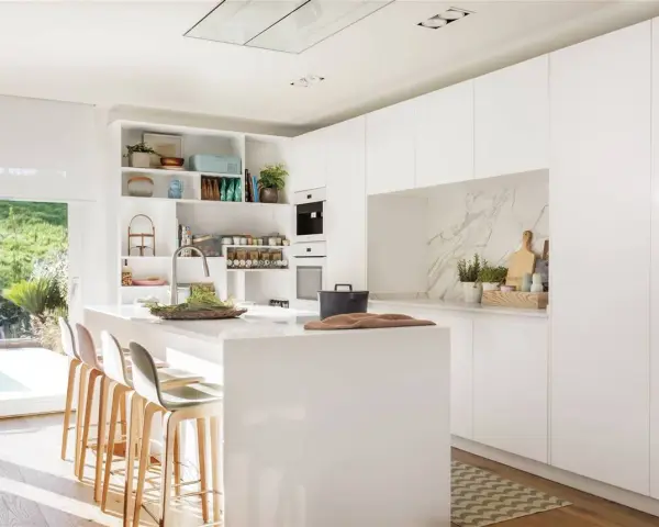 Cocina blanca moderna con isla central, estanterías abiertas y vistas al jardín. Ideas para decorar pared cocina blanca con estilo minimalista.