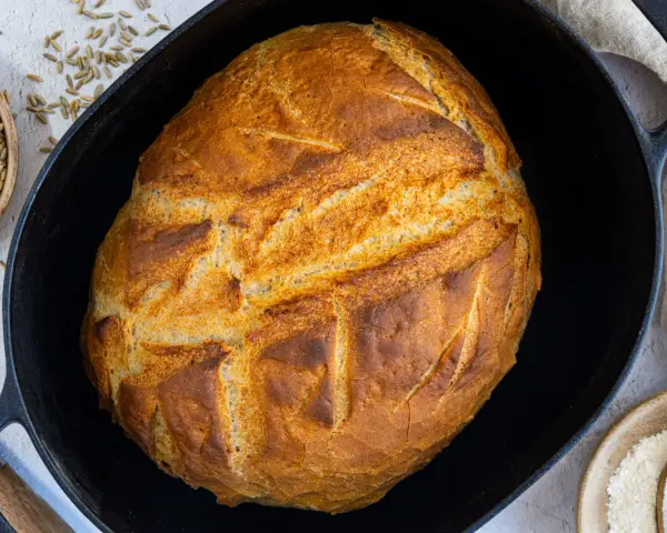 Ein goldbraunes Brot mit knuspriger Kruste liegt in einem Gusseisentopf. Dieses Brot kommt nicht aus dem Topf, sondern wurde darin gebacken.