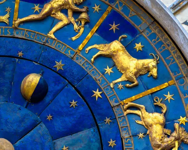 Złoty koziorożec na niebieskiej tarczy zegara astronomicznego, otoczony gwiazdami i cyframi. Dlaczego koziorożec milczy? Może czeka na swój czas.