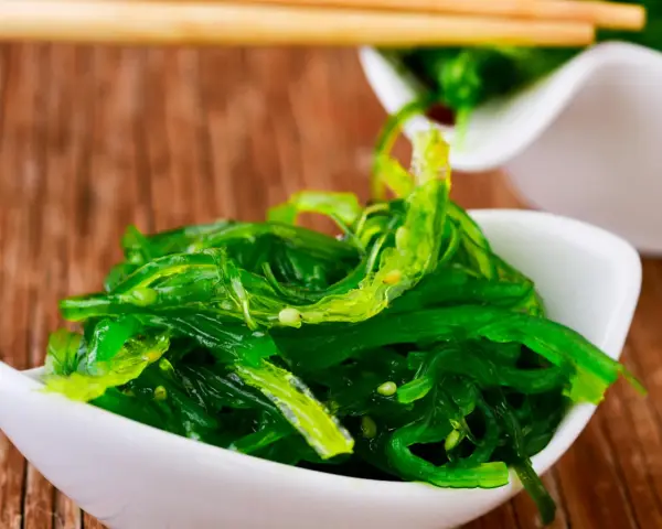 Salade d'algue de mer verte et brillante, servie dans un bol blanc, prête à être dégustée avec des baguettes.