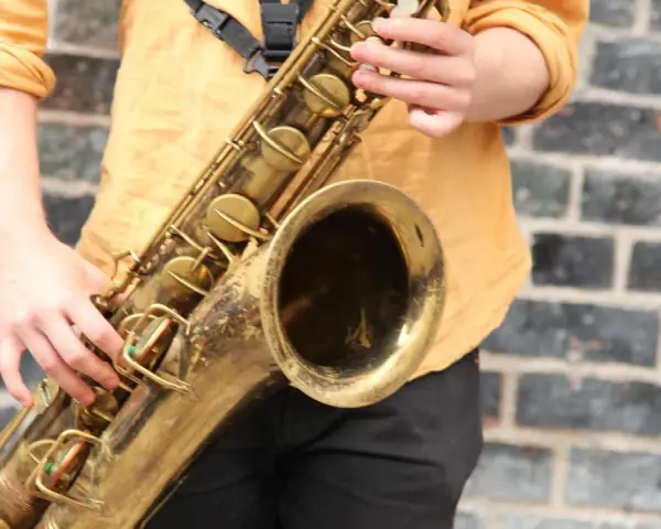 Hände spielen ein goldenes Saxophon. Obwohl es aus Metall ist, ist das Saxophon ein Holzblasinstrument, da der Ton durch ein Rohrblatt erzeugt wird.