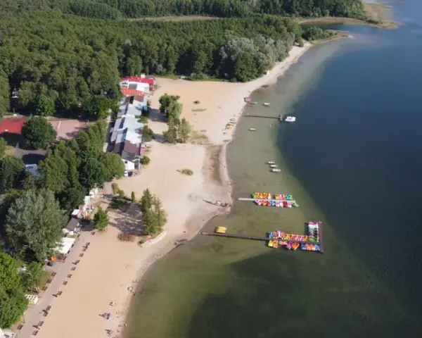 Skorzęcin jezioro z lotu ptaka: piaszczysta plaża, kolorowe rowery wodne, budynki i las.