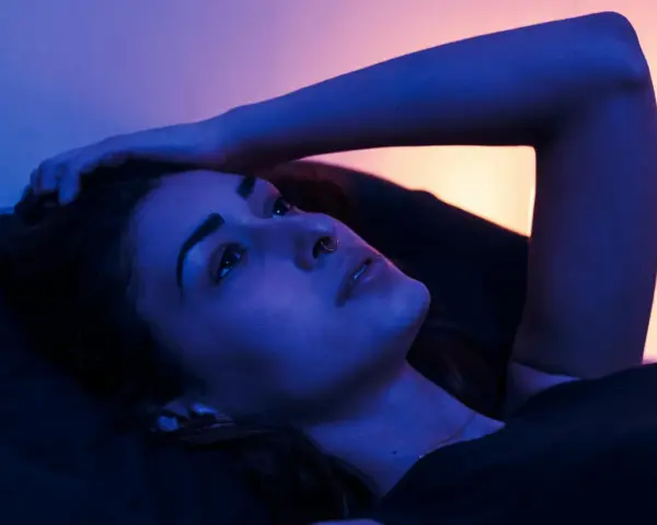 Młoda kobieta leży w łóżku, ręka oparta o głowę. Nocne światło tworzy intymną atmosferę, idealną na seks po kryjomu.