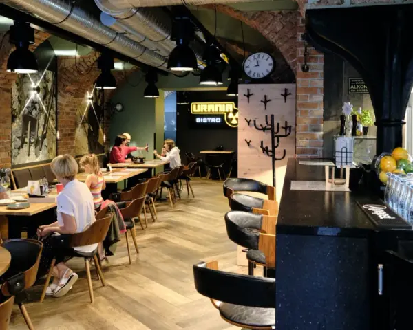 Wnętrze restauracji Urania Bistro z ludźmi przy stołach i barem.