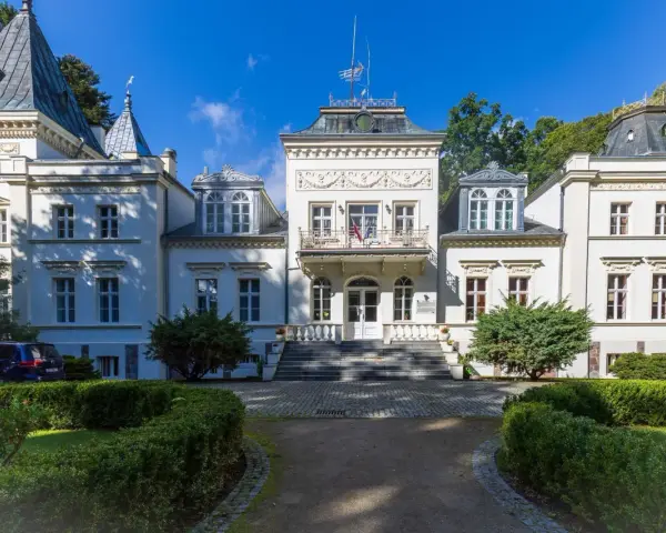 Elegancki pałac w Nosowie z wieżyczkami i ozdobnym balkonem, otoczony zielenią.