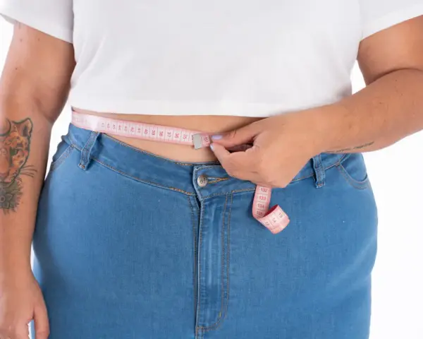 Persona plus size se mide la cintura con una cinta métrica rosa.