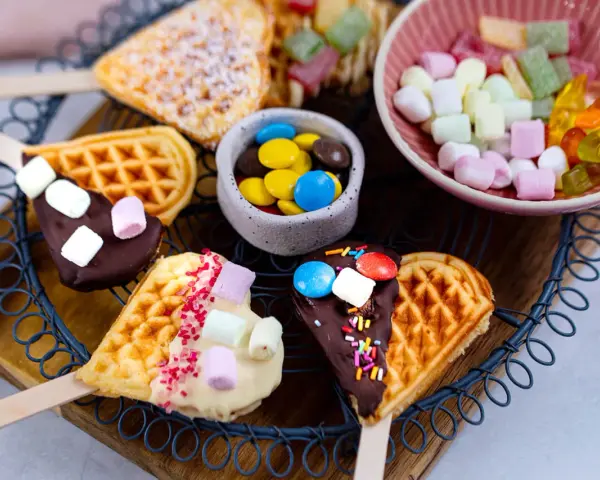 Herzförmige Waffeln am Stiel, dekoriert mit Schokolade, Marshmallows und Streuseln. Ein süßes Rezept für Waffeln am Stiel!