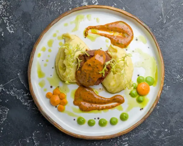 Mięso z puree ziemniaczanym, ozdobione pomarańczowym sosem do mielonych i zielonymi groszkami.