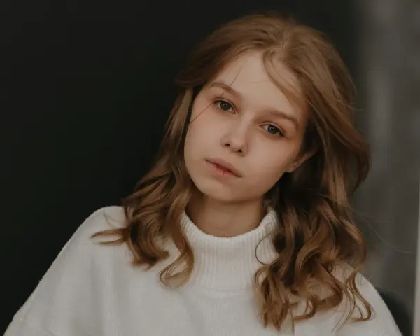 Młoda dziewczyna z burzą brązowych włosów, w białym golfie, zamyślona. Zastanawia się, jak przeprosić dziewczynę, by naprawić błąd.