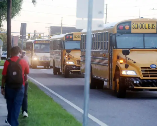 Schüler gehen zur Schule, während gelbe Schulbusse vorbeifahren. Denken Sie über die Kosten nach: wie viel kostet ein Auslandsjahr in Amerika?