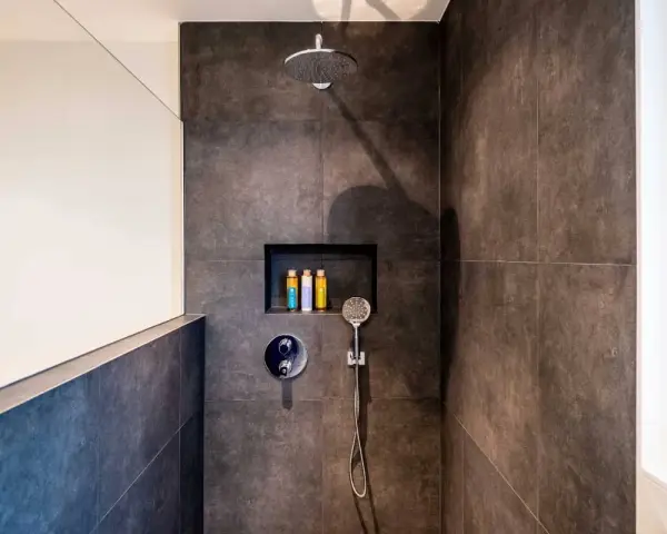 Ducha moderna con tabique de obra y muro de cristal. Incluye alcachofa de lluvia, grifería empotrada y nicho con botes de champú.