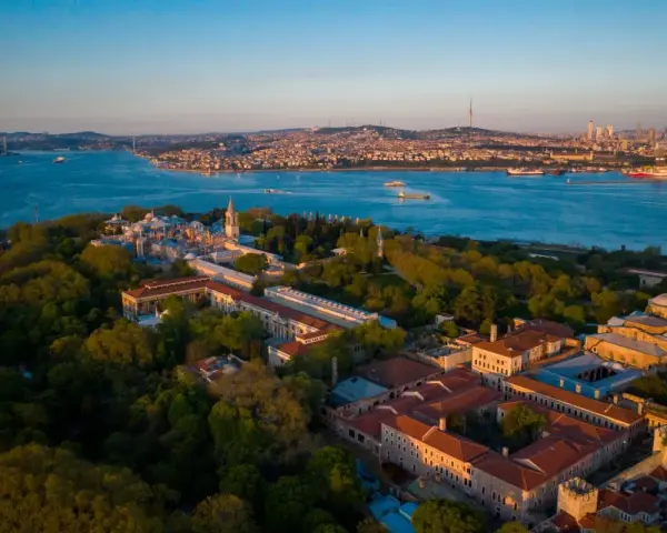Aerial view of the Topkapi Palast complex, nestled amongst lush greenery, with the Bosphorus Strait and Istanbul skyline in the background.