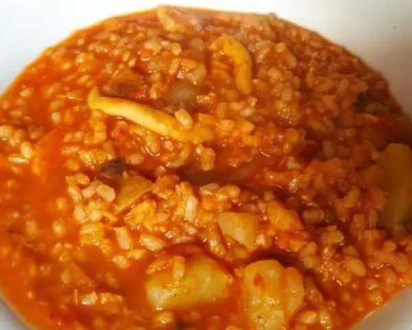Arroz caldoso con trozos de marisco y verduras en salsa rojiza.