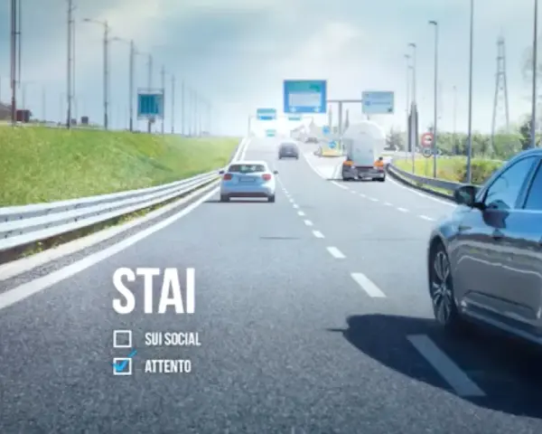 Sulla strada, auto e camion procedono. "STAI ATTENTO" è scritto, ricordando l'art. 79 CDS.