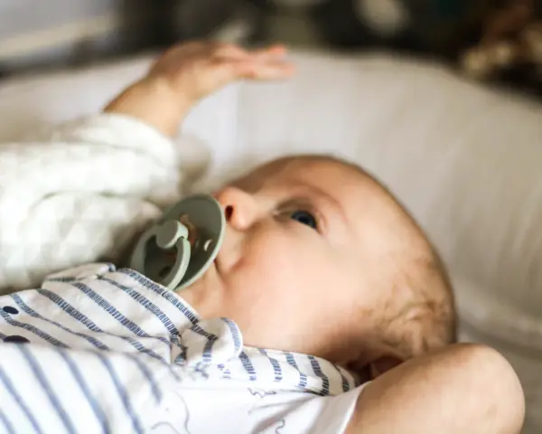 Uroczy noworodek z niebieskimi oczami i smoczkiem. Sprawdzam temperaturę noworodka na czole, by upewnić się, że jest mu komfortowo.