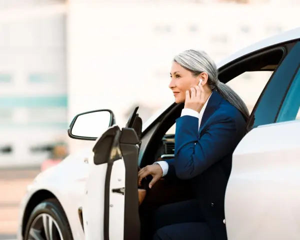 Elegancka kobieta w garniturze wsiada do białego auta. To jej auto na abonament, idealne do biznesowych podróży.