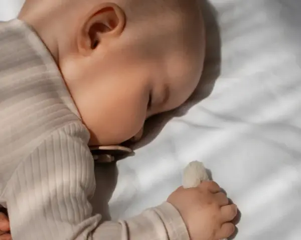 Bambino dorme sereno, forse grazie alla melatonina per bambini iperattivi, con ciuccio e peluche.
