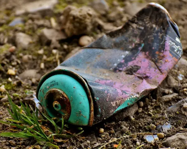 Lata de aerosol aplastada y oxidada en el suelo, un ejemplo de las causas de la contaminación.