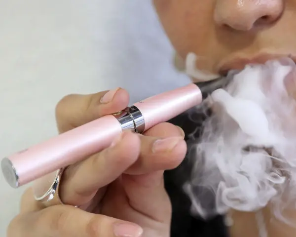 Persona exhala vapor de un cigarrillo electrónico rosa. ¿Qué es peor el vaper o el tabaco?