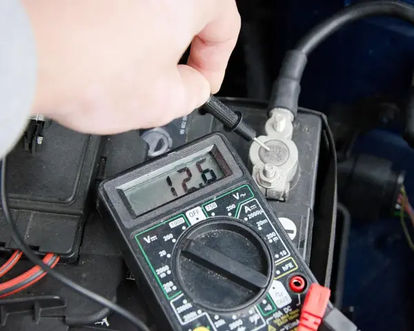 Sprawdzanie prawidłowego napięcia akumulatora multimetrem. Wynik 12.6V wskazuje na dobry stan.