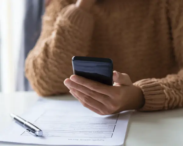 Persona revisa su teléfono móvil, modelo 035, mientras tiene un bolígrafo y un formulario de solicitud sobre la mesa.