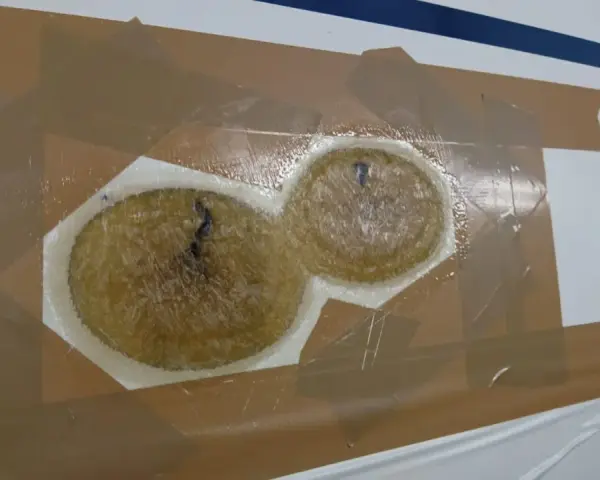 Reparaturstelle an einem Boot, bereit für das gelcoat erneuern. Zwei runde, faserige Füllungen sind mit Klebeband abgedeckt.