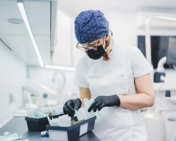 Dentystka w czepku i masce przygotowuje materiały, w tym te do zabiegów z użyciem abrazji powietrznej.