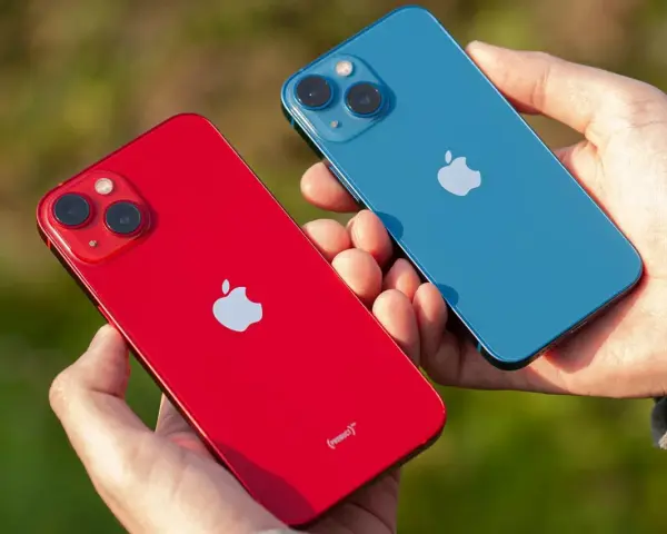 Dwie dłonie trzymają dwa telefony: czerwony i niebieski iPhone 13 mini. Aparat obu modeli jest widoczny.