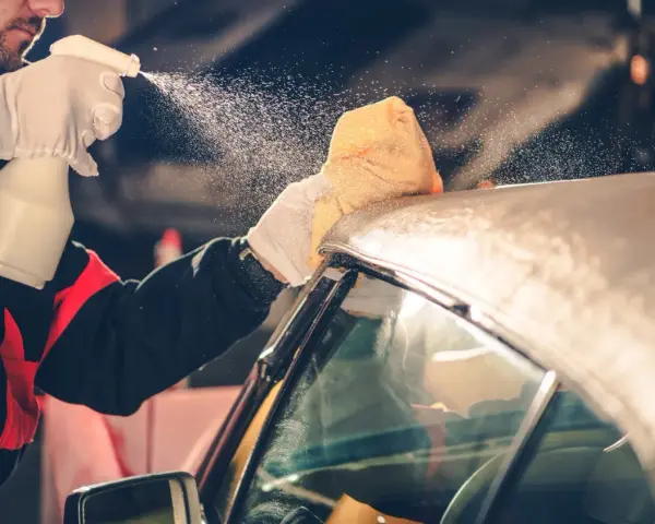 A person in gloves sprays a convertible car's fabric top with cleaning solution, then wipes it with a sponge. This is how you wash a convertible car.