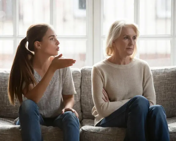 Junge Frau gestikuliert wütend, während ihre Mutter abgewandt sitzt. Es scheint, als ob meine Tochter mich hasst.