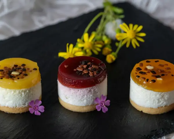 Efektowne ciasto bez pieczenia: trzy mini deserki z galaretką, kremem i owocami, ozdobione kwiatami i czekoladą.