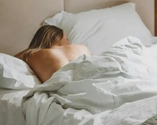 Une femme se repose dans un lit défait, la peau nue exposée, évoquant un désir sexuel latent.