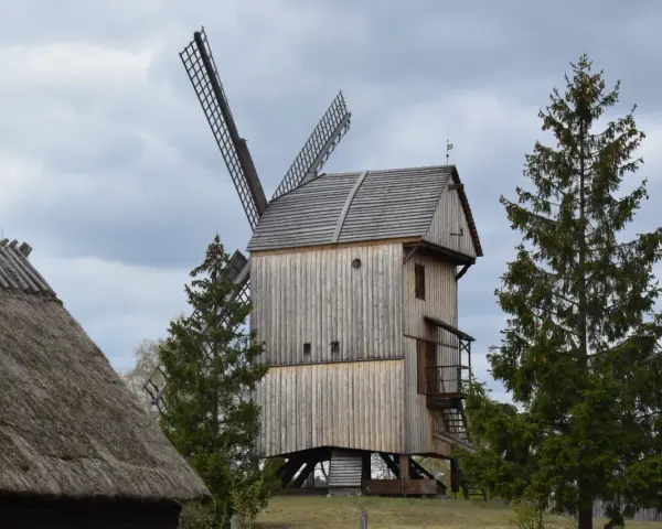 Wiatrak w skansenie Kaszuby, drewniany, z widocznymi skrzydłami i strzechą na dachu.