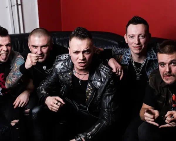 Pięciu mężczyzn w skórzanych kurtkach i z rockowymi fryzurami, jakby gotowi na nocny koncert. Wyglądają jak zespół nocny kochanek.