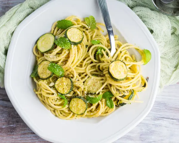 Spaghetti con zucchine cremosa, guarniti con foglie di menta fresca e parmigiano grattugiato. Un piatto leggero e gustoso.