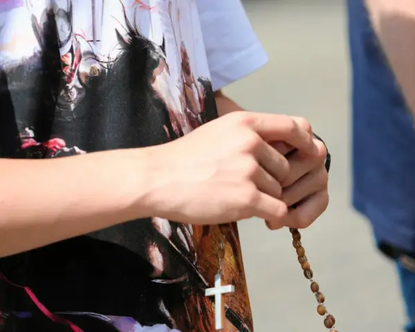 Dłoń trzyma paciorki różańca, a na koszulce widnieje biały krzyż. To znak modlitwy, żeby się wszystko ułożyło.