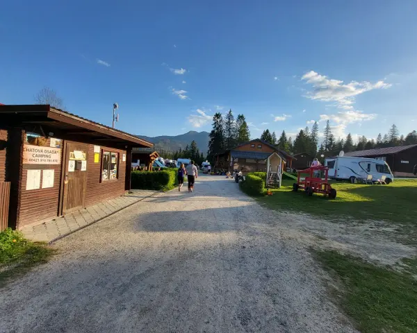 Słoneczny dzień na **camping Oravice**. Drewniany budynek recepcji, przyczepy kempingowe i zielone wzgórza w tle.