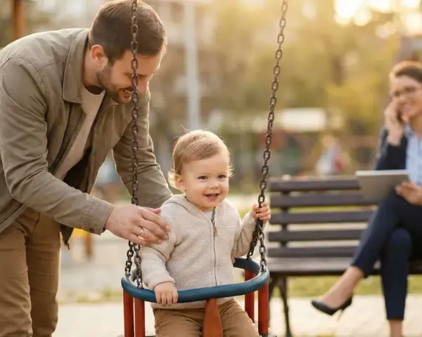Ein Vater schaukelt sein Kind. Im Hintergrund telefoniert eine Frau. Die Frage, an welchen Kosten sich der Vater beteiligen muss, bleibt offen.