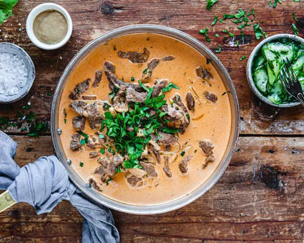 En krämig biff stroganoff med färsk persilja, serverad med gurksallad och en liten skål med senap. Perfekt vin till biff stroganoff.