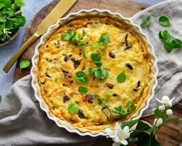En gyllene kantarellpaj, perfekt för ett höstligt kantarellpaj recept. Garnerad med färska gröna blad och serverad med en gyllene kniv.