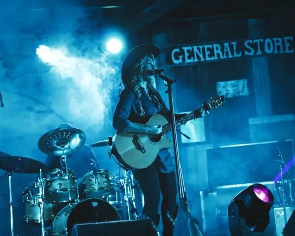 Artystka w kapeluszu gra na gitarze, wykonując najpopularniejsze piosenki country. W tle perkusja i napis "GENERAL STORE".
