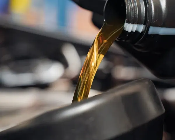 Goldfarbenes Motoröl fließt aus einem schwarzen Behälter in einen dunklen Trichter.