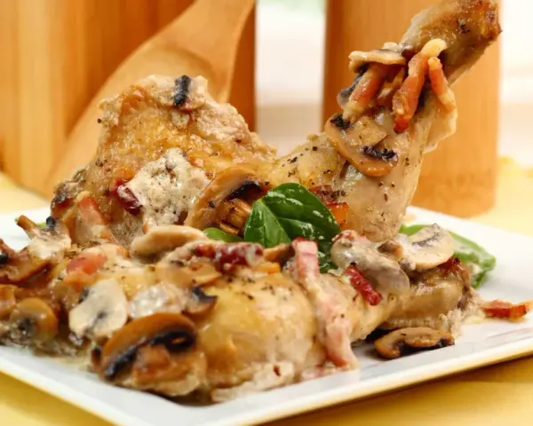 Delicioso pollo con champiñones y tocino en una cremosa salsa, servido en un plato blanco.