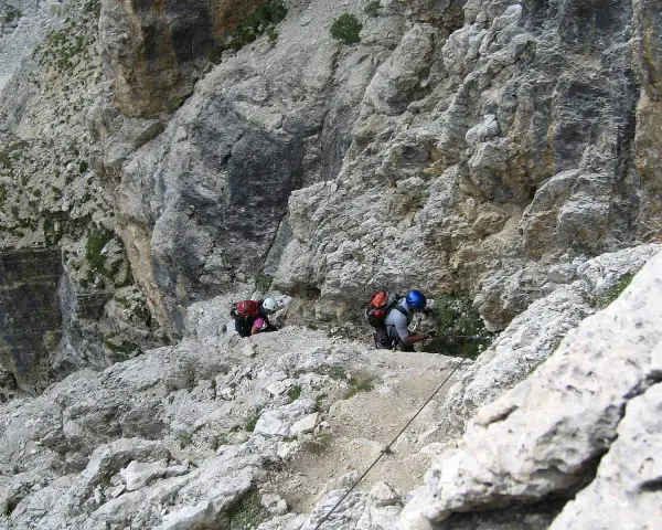 Dwóch turystów pokonuje via ferraty w Dolomitach, wspierając się na stalowej linie.