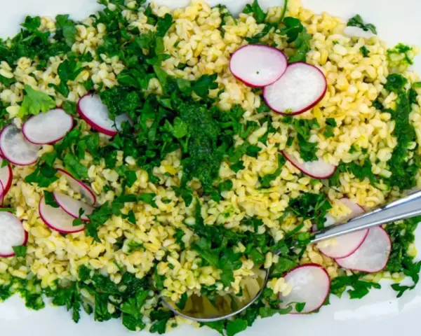 En fräsch bulgursallad med rädisor och färska örter, serverad på en vit tallrik med en sked.