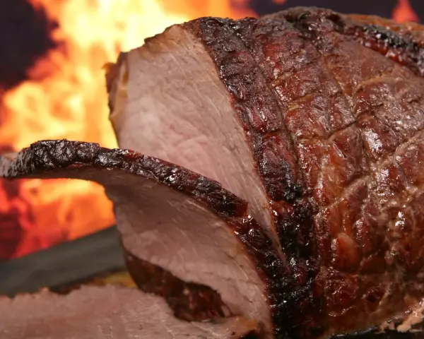 Un enchaud de porc juteux, rôti à la perfection, avec une croûte caramélisée et des flammes dans l'arrière-plan.