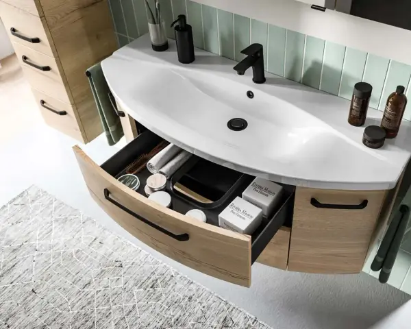 Aménagement salle de bain moderne avec lavabo blanc, robinetterie noire et tiroirs en bois clair organisés.