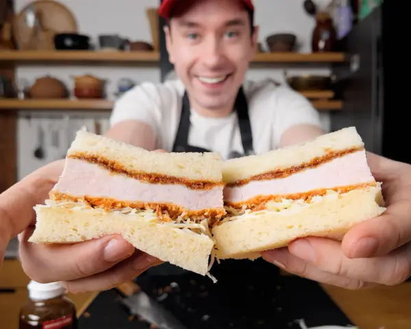 Uśmiechnięty mężczyzna prezentuje pyszne katsu sando z soczystym kotletem schabowym w panierce, delikatną kapustą i puszystym chlebem.
