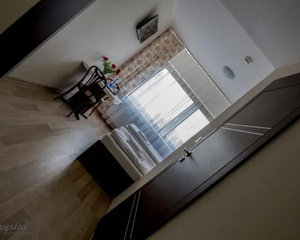 Pokój w hotelu i restauracji Crystal: łóżko, stolik z krzesłami i kwiatami, okno z zasłonami.