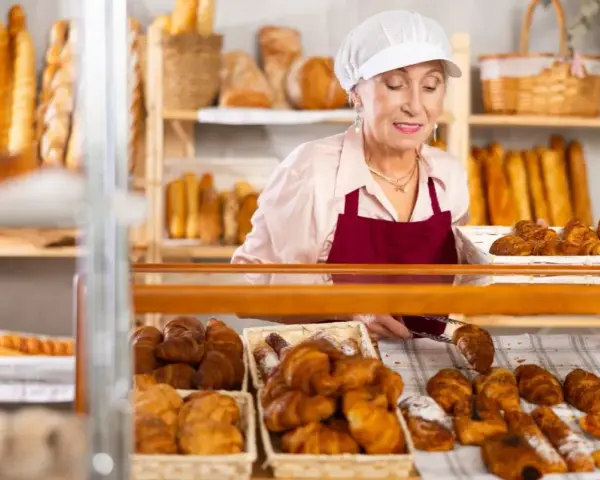 Starsza pani piekarz z uśmiechem układa świeże croissanty. To ulga dla pracujących seniorów, którzy wciąż mają pasję.